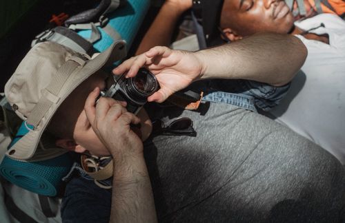 Free From above of anonymous male traveler taking photo on camera while lying near crop napping African American partner Stock Photo