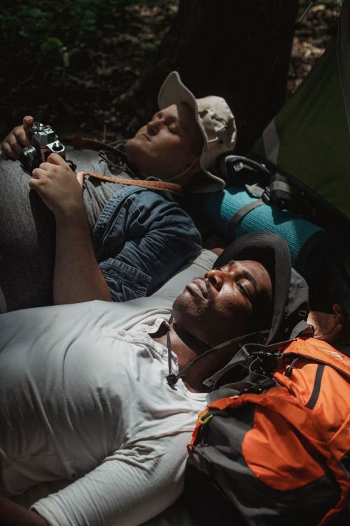 Free From above of young multiethnic male partners in panama hats lying on backpacks during hike Stock Photo