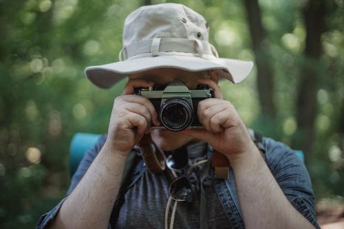 Free Unrecognizable male traveler taking photo on camera during trip in summer forest on weekend Stock Photo