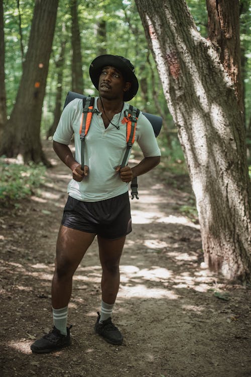 Young contemplative African American tourist looking up on path in summer forest during trip