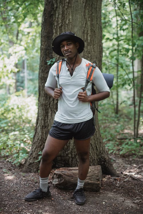 Free Young black male traveler with rucksack looking at camera on path near tree trunk in woods Stock Photo