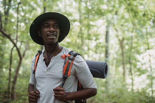 Free Dreamy black male traveler with backpack in woods Stock Photo