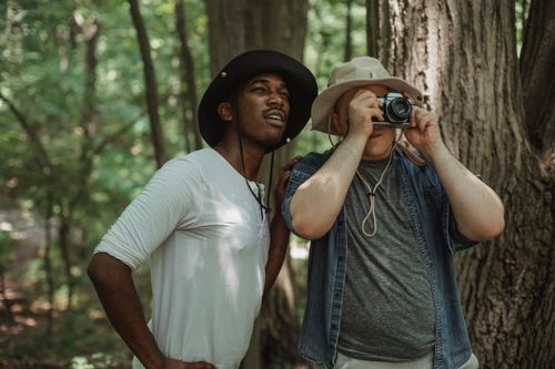 Free Male traveler taking photo on camera near African American partner during trip in woods Stock Photo