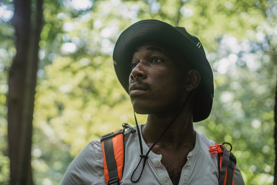 Serious young black guy standing in forest during hiking trip