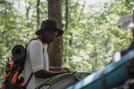 Concentrating young black guy setting up camping tent in woods