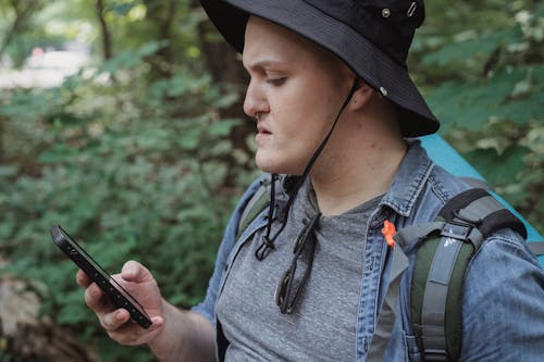 免費 重點檢查年輕男性背包客在自然中檢查智能手機的位置 圖庫相片