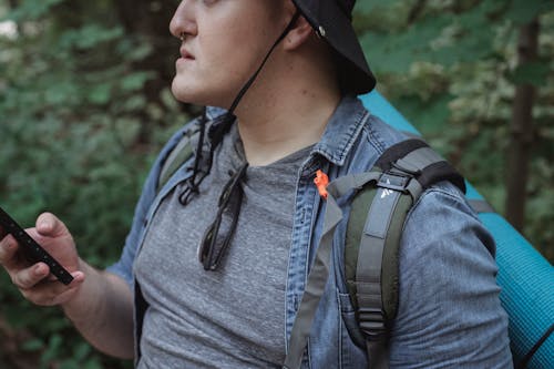 Crop male hiker with smartphone in woods