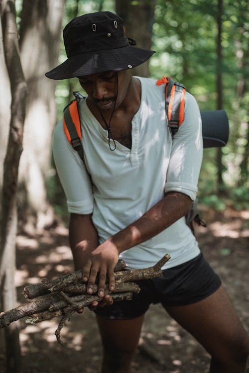 African American backpacker in casual wear standing with dry twigs on pathway in woods