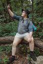 一位徒步旅行者坐在树林的树干上，在夏季徒步时自拍