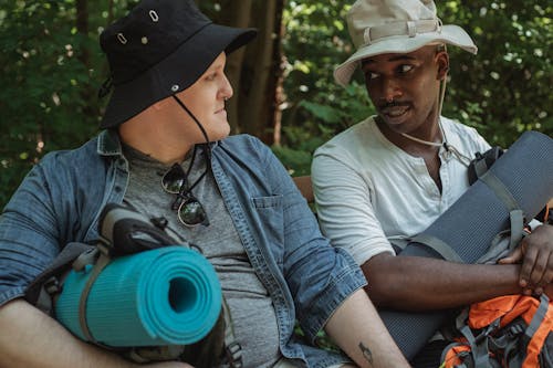 Crop diverse friends with hiking equipment talking in forest