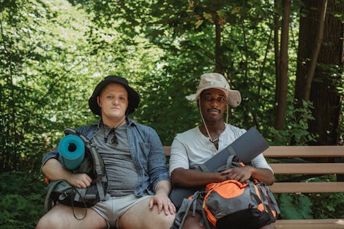 Multiethnic friends with rucksacks resting on bench in forest