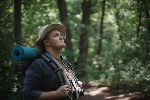 мечтательный турист мужчина с походным снаряжением исследует зеленый лес