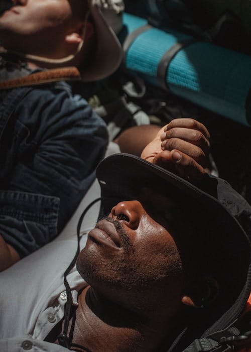 From above multiracial men covering eyes with hats and sleeping in camp tent after intense trekking