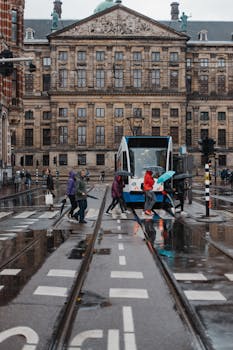 在历史建筑的背景下，人们穿过电车前的潮湿街道