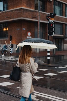 Woman walking with an umbrella on a rainy urban street, city traffic in the background.