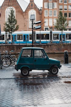 A vintage green car parked on a wet street with a tram in the background in Amsterdam.