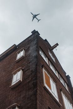 一架飞机在多云的天空下飞过一座高大的砖砌建筑，从下方被捕捉到