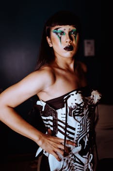 一位自信的亚洲女性在室内展示着她创意十足、色彩缤纷的妆容与艺术服装，散发着独特的个性