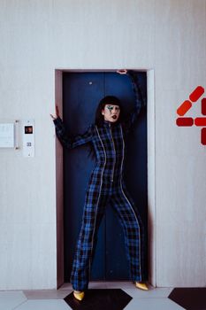 一位亚洲女性身穿方格服装，脸上绘有人体艺术，正举起手臂站在电梯门附近