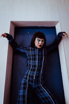 From below of Asian female with body art on face looking at camera while standing with raised arms near doors of elevator