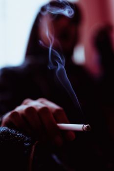 一个模糊的匿名女子坐在房间靠窗的墙边，手里拿着香烟，在烟雾中吸着烟