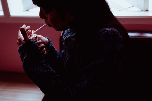 一位时尚女性在氛围多变的室内点燃香烟，优雅而沉思