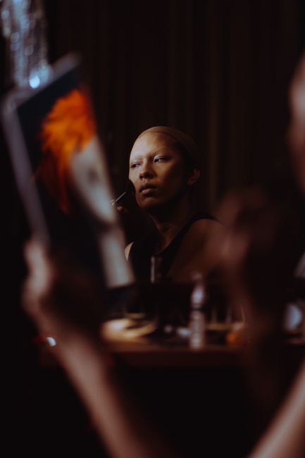 Young ethnic female applying beige foundation and powder on face while admiring makeup in mirror