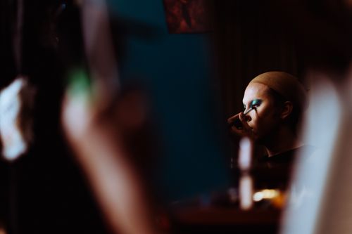 Free Side view of young theater artist in wig cap applying makeup on face with applicator Stock Photo