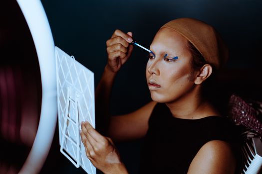 Young focused ethnic female applying cosmetic with applicator on eyelids and looking at mirror