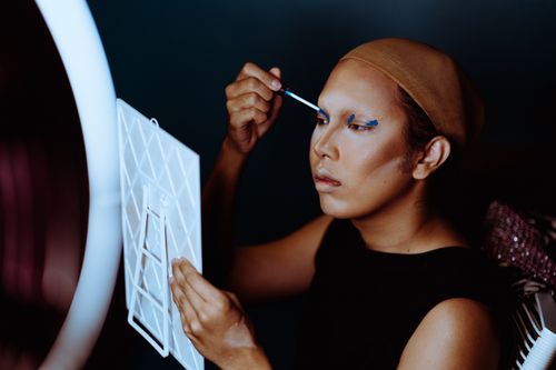 Free Young focused ethnic female applying cosmetic with applicator on eyelids and looking at mirror Stock Photo