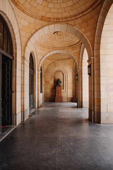 Explore a gothic arched hallway featuring a classical bust statue within an ancient stone architecture.