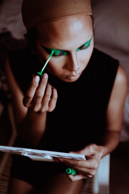 Crop ethnic woman applying green eye shadow on eyelid