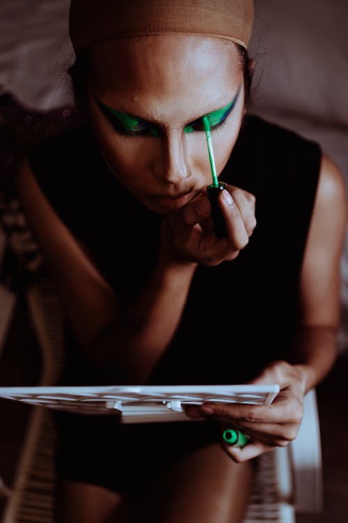 From above of crop young ethnic woman with mirror applying makeup on face in room