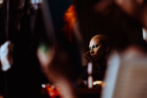 Free Side view of young female theater artist applying bright eye shadow on eyelid using cosmetic brush in makeup room Stock Photo