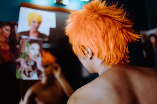 Back view of anonymous ethnic naked androgynous male stylist looking at mirror under LED lamp