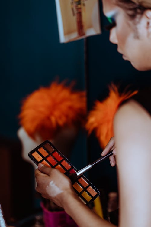 Side view of crop ethnic female artist doing make up with brush in dressing room