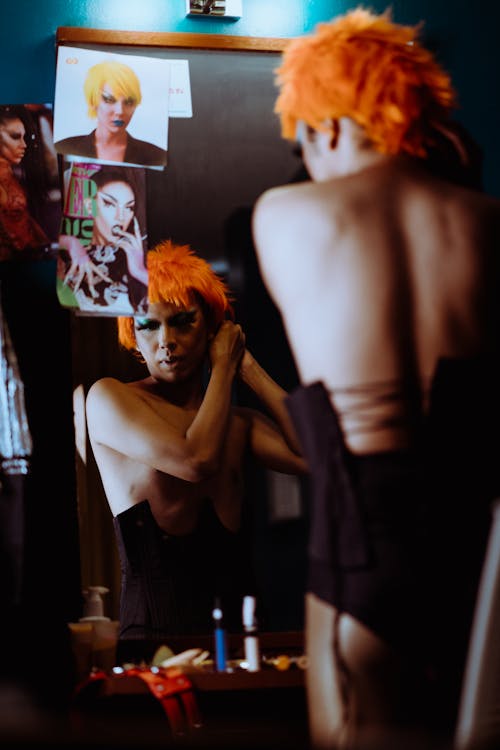 Low angle back view of ethnic man with makeup in wig and tightly fitting underwear reflecting in mirror