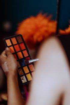 Back view of crop ethnic female doing makeup with brush and eyeshadows in studio