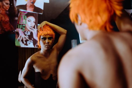Back view of ethnic man looking at reflection in mirror while creating feminine appearance of cover model