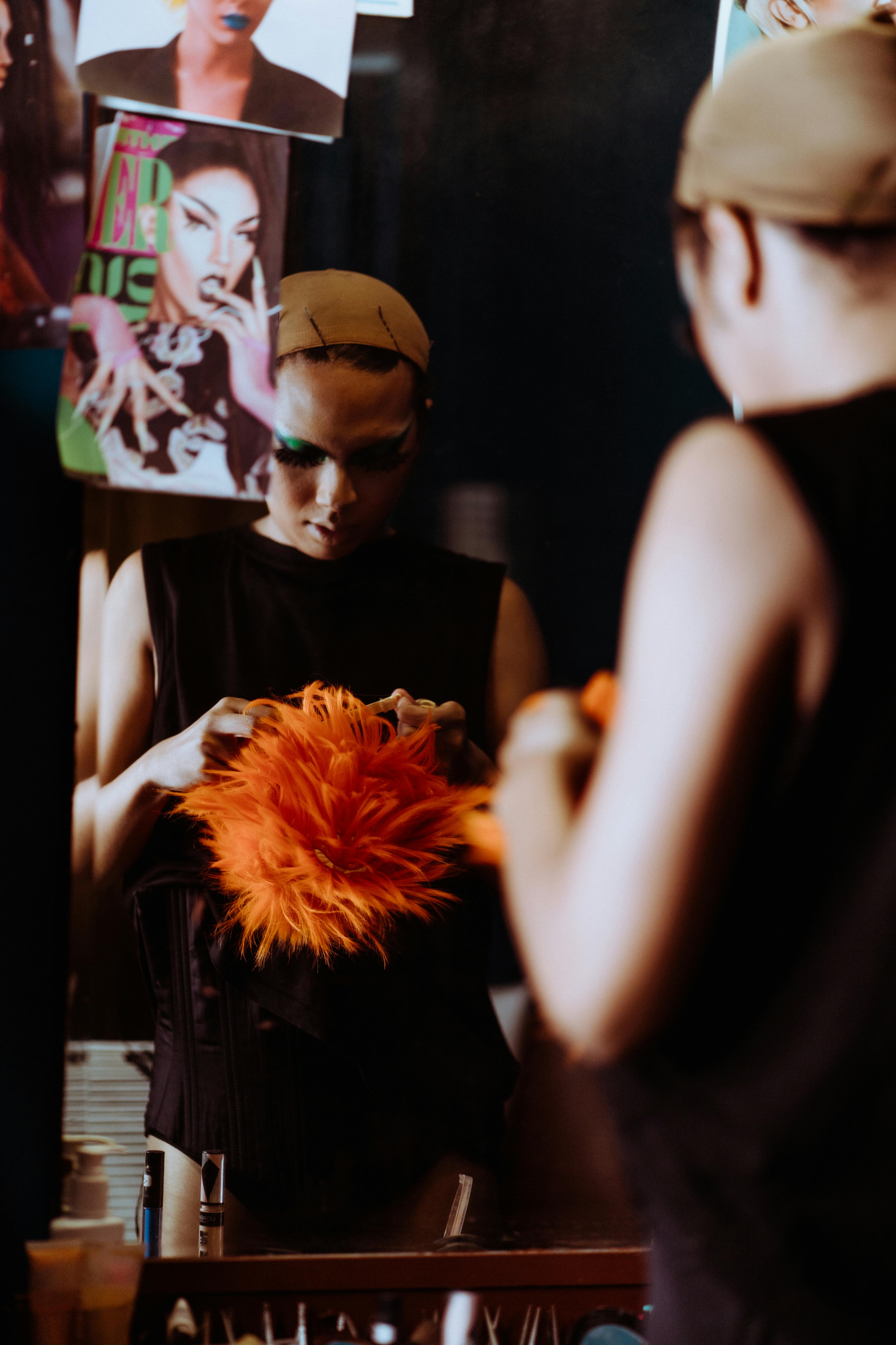 Free Drag performer adjusting orange wig in a chic dressing room setting, reflecting artistic expression. Stock Photo