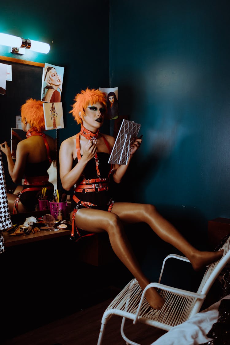 Sensual Young Transsexual Guy In BDSM Clothes Sitting In Dressing Room Near Mirror