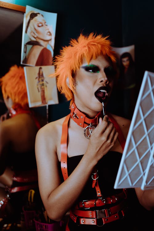 Sensual young ethnic transsexual male artist in BDSM outfit applying makeup in dressing room