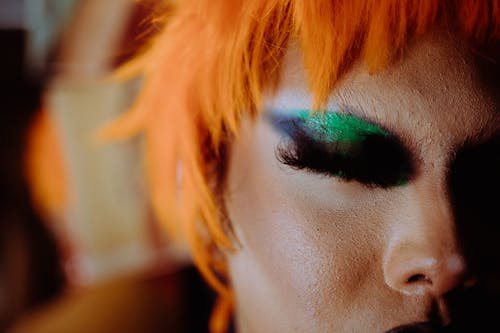 Unrecognizable eccentric person with orange hair and bright makeup