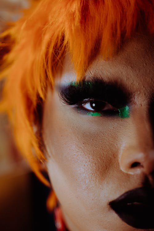 Closeup of crop extravagant ethnic androgynous person with bright makeup and wig looking at camera
