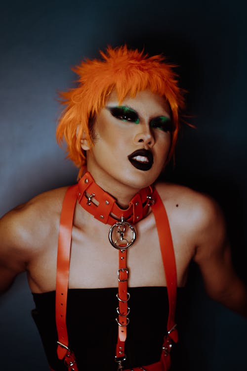 Seductive young ethnic androgynous guy with artistic makeup in BDSM costume in studio