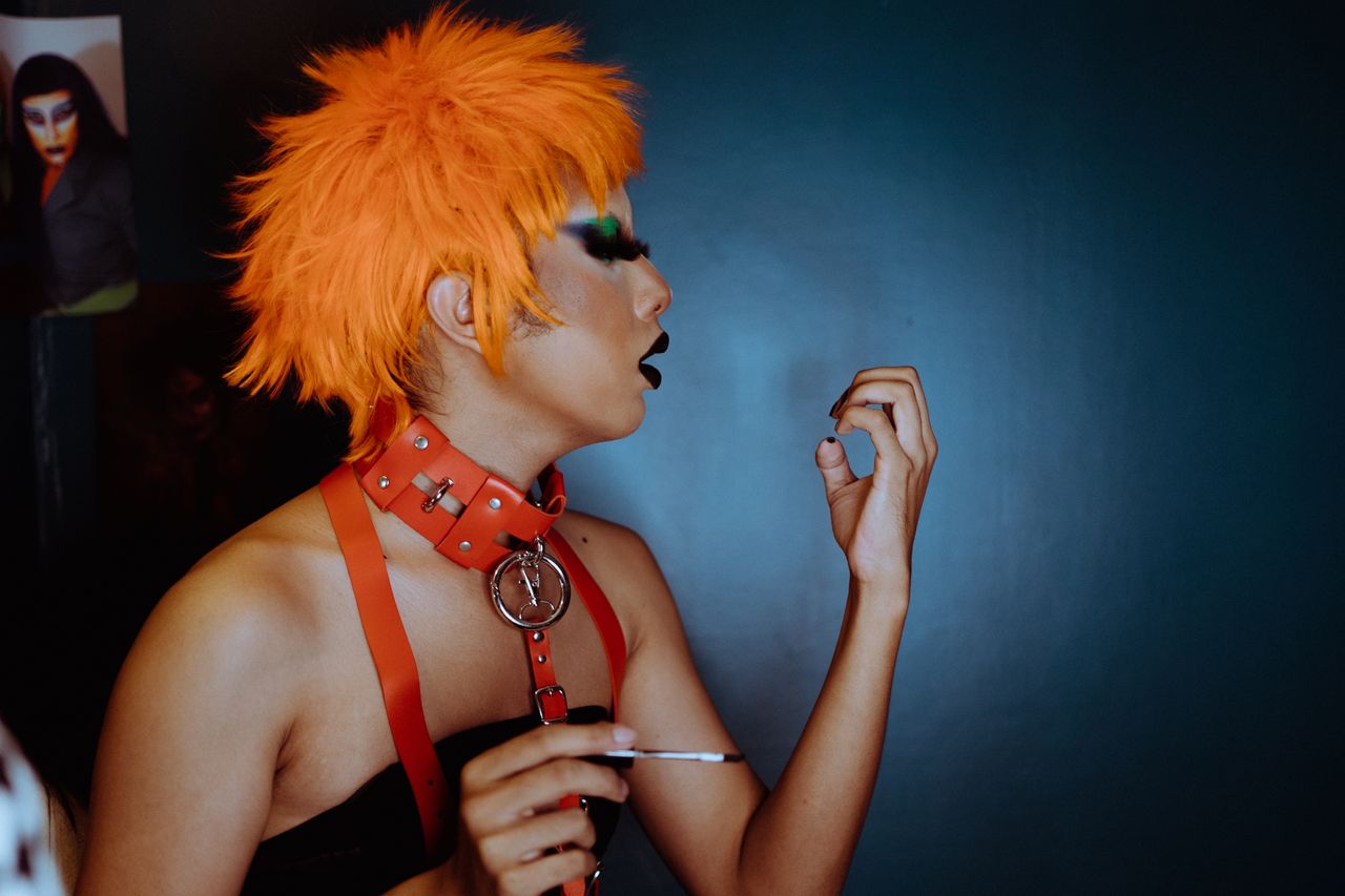 side view transgender male with orange dyed hair and dark makeup blowi