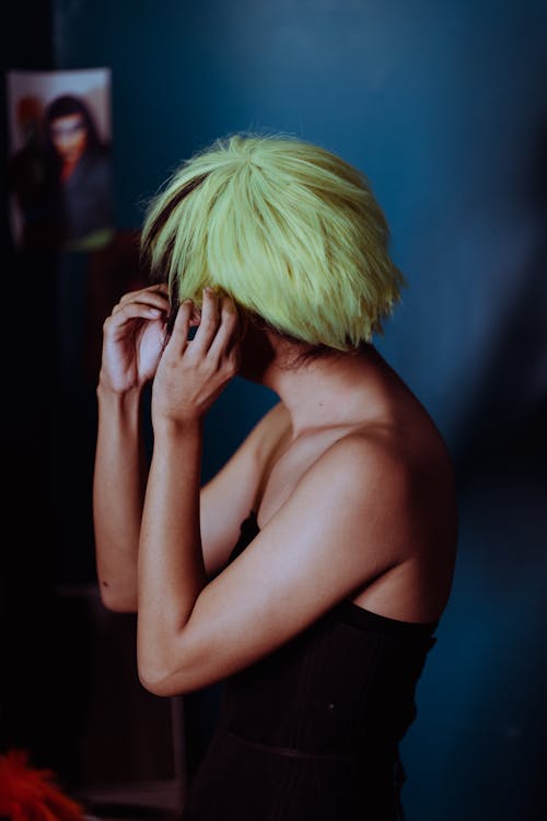 Side view of anonymous female theater artist putting on wig with green hair in dressing room