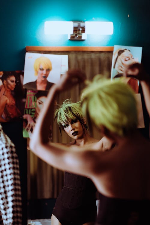 Back view of female theater artist with makeup putting on wig while reflecting in mirror in dressing room