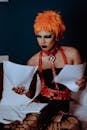 Young ethnic female artist with bright makeup in bondage learning role from script on papers while sitting on bed