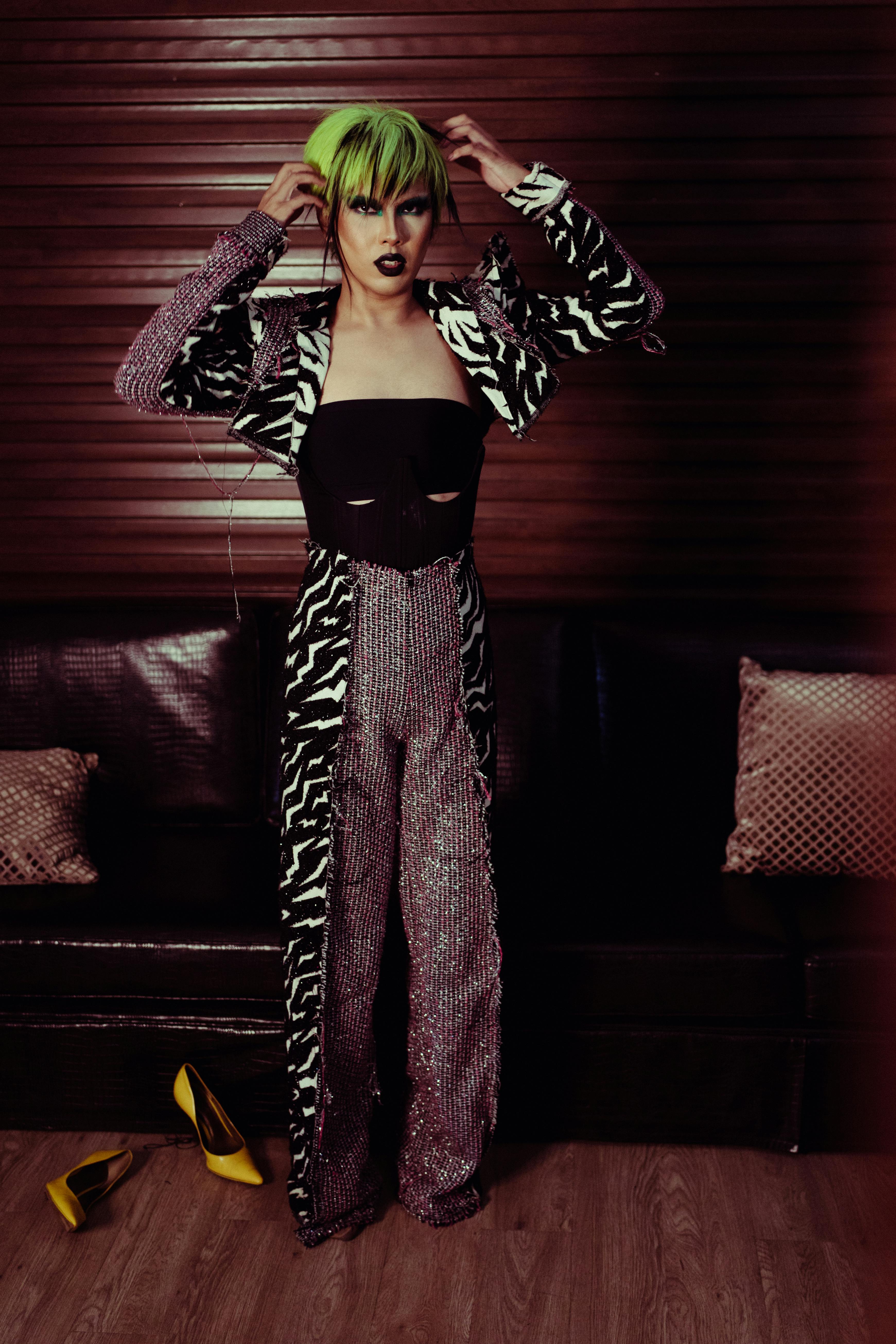 Young extravagant female theater artist with makeup touching artificial green hair while looking at camera at work